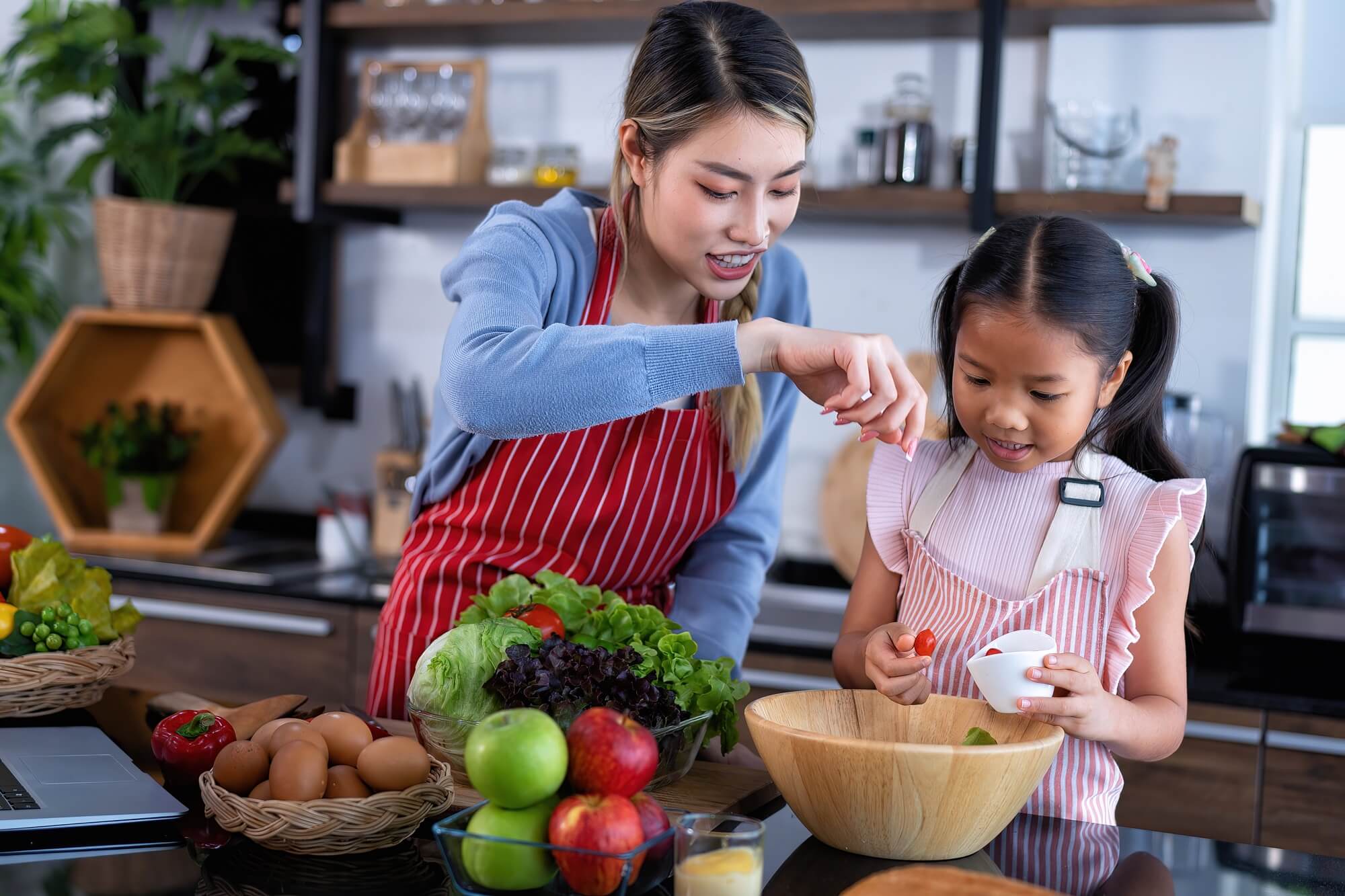 Young mother teach daughter cooking clean food from laptop